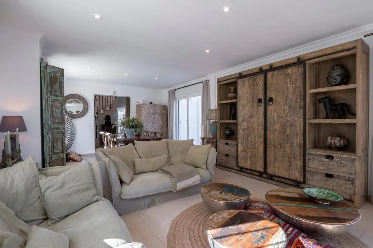 Séjour doté d'un grand meuble mural en bois rustique, de canapés en lin beige et de tables basses circulaires en bois de récupération sur un tapis en jute.
