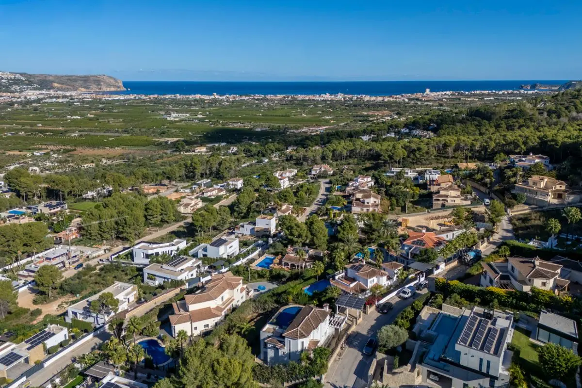Vue aérienne d'un quartier résidentiel vallonné comprenant des villas avec piscines et panneaux solaires, surplombant la vallée et le littoral.