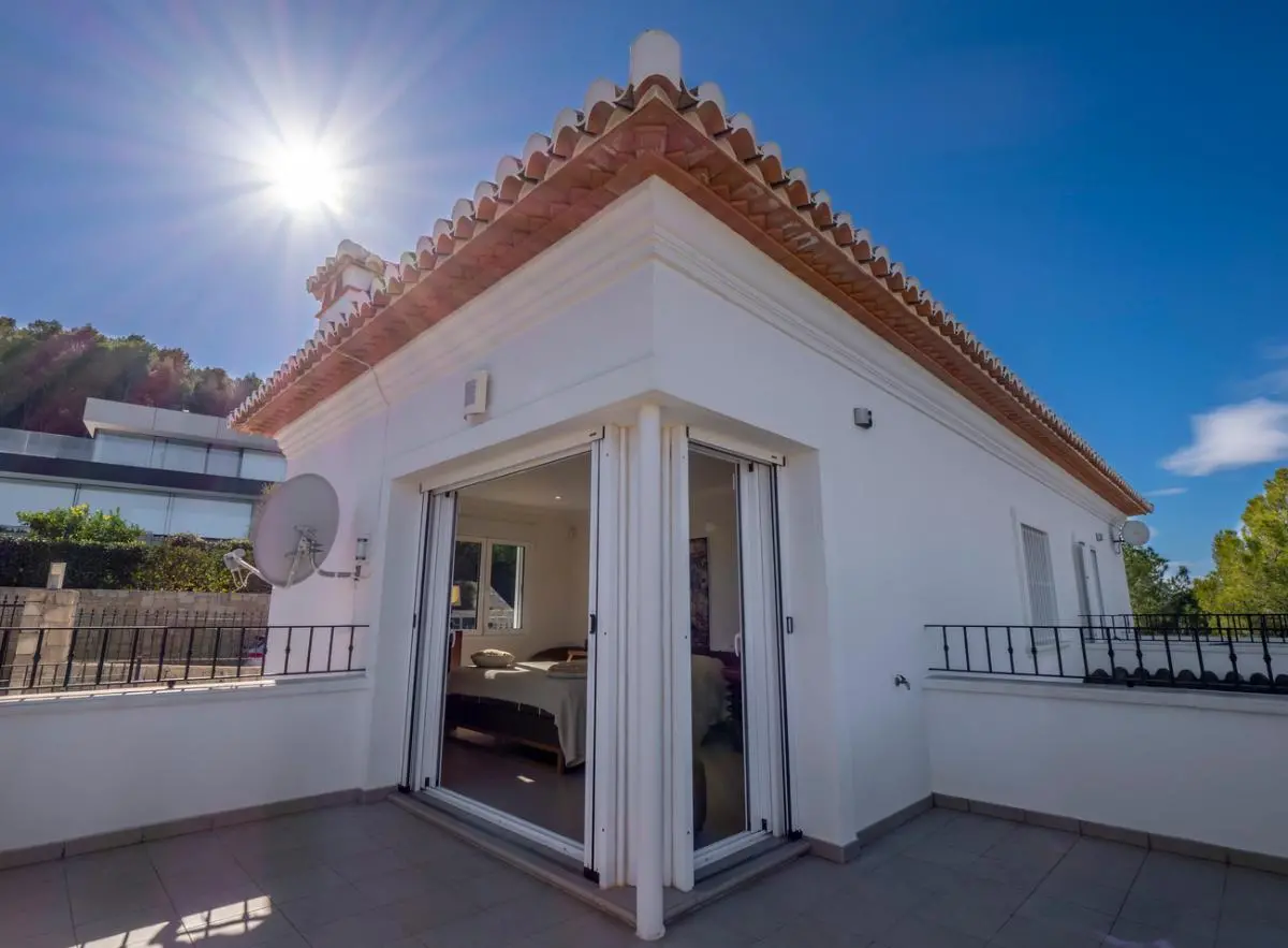 Vue extérieure d'une chambre à l'étage avec de grandes baies vitrées coulissantes ouvrant sur une terrasse privée carrelée sous un toit en tuiles.