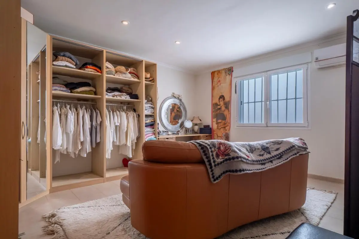 Zone de dressing spacieuse avec rangements en bois ouverts, canapé en cuir fauve et coiffeuse avec miroir circulaire sous un éclairage encastré.