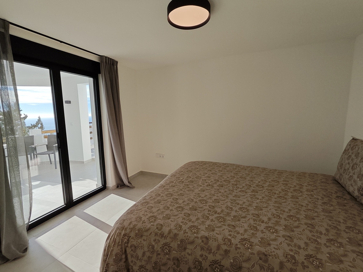 Chambre avec lit double, parure florale et accès direct à une terrasse privée offrant une vue sur la mer via de larges baies vitrées.
