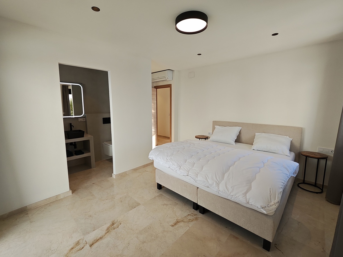 Chambre moderne avec sol en marbre, lit double rembourré et salle de bain attenante équipée d'une vasque noire et d'un miroir rétroéclairé.