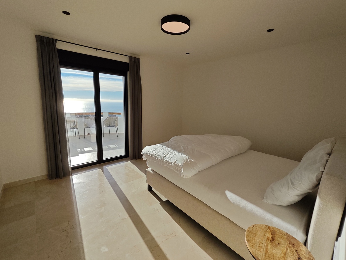 Chambre moderne avec sol en marbre poli, lit double et grandes baies vitrées s'ouvrant sur une terrasse privée avec vue sur l'océan.