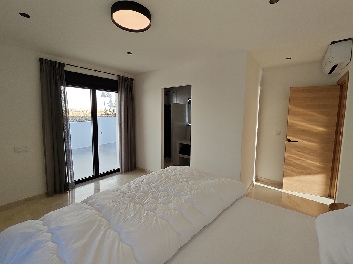Chambre moderne avec sol en pierre polie, accès direct à la terrasse par une baie vitrée et salle de bain attenante intégrée.
