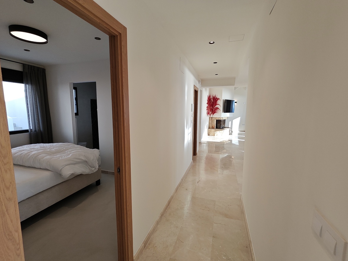 Couloir lumineux avec sol en marbre poli menant à un salon avec cheminée en pierre, offrant une vue sur une chambre aux finitions en bois.