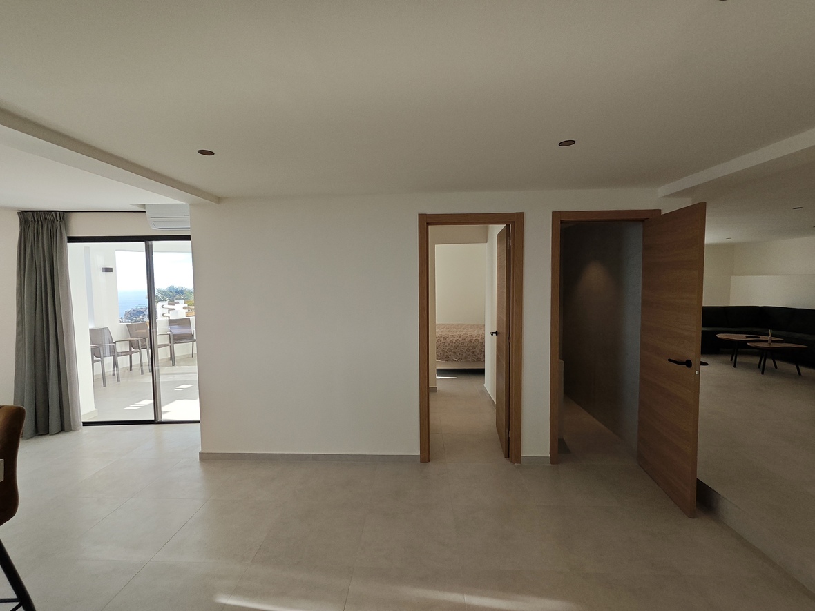 Dégagement intérieur avec carrelage clair, portes en bois naturel et accès par baie vitrée à une terrasse offrant une vue sur l'océan.