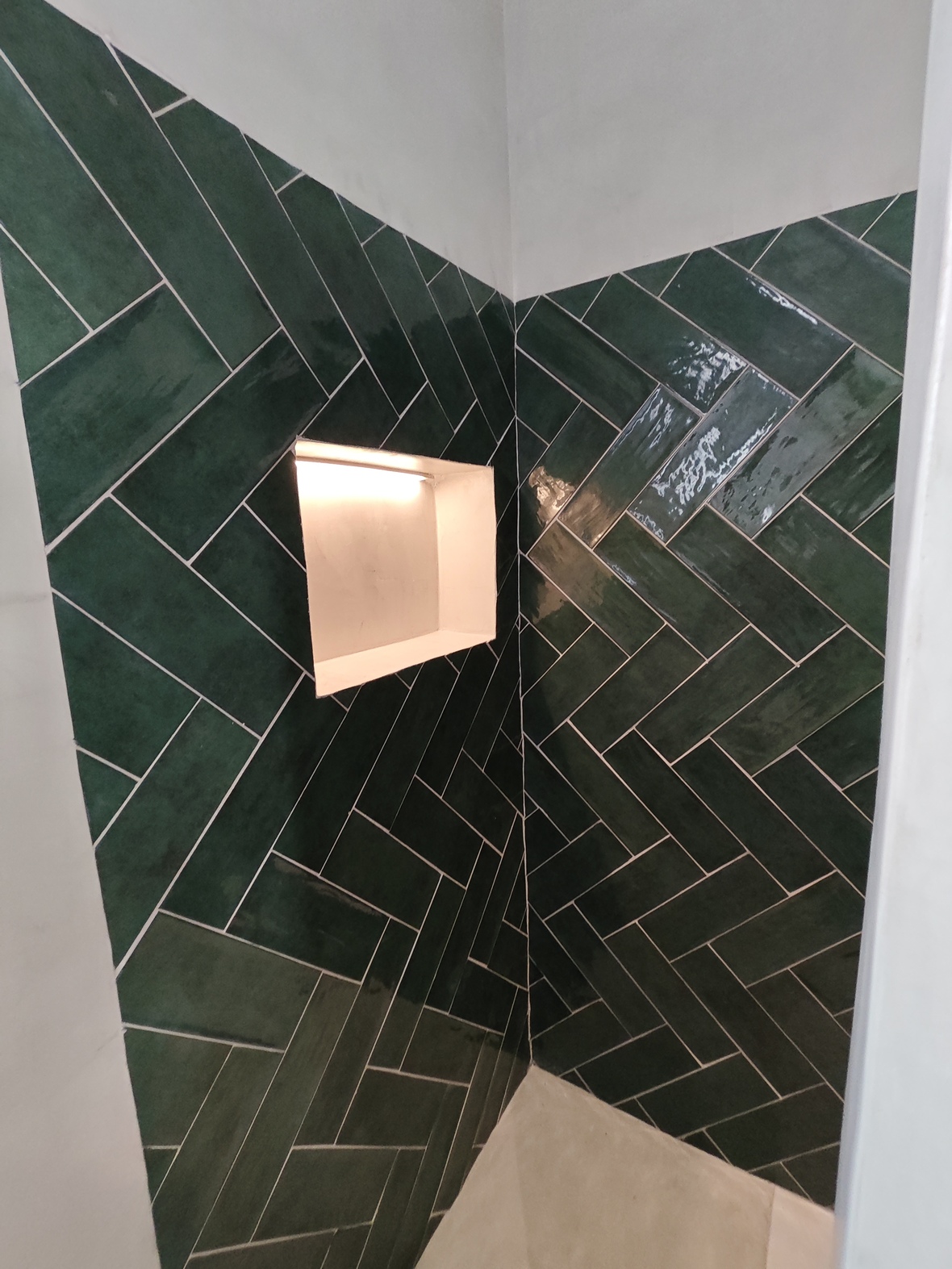 Détail d'un coin douche avec carreaux vert émeraude en chevrons et une niche murale encastrée dotée d'un éclairage LED chaleureux.