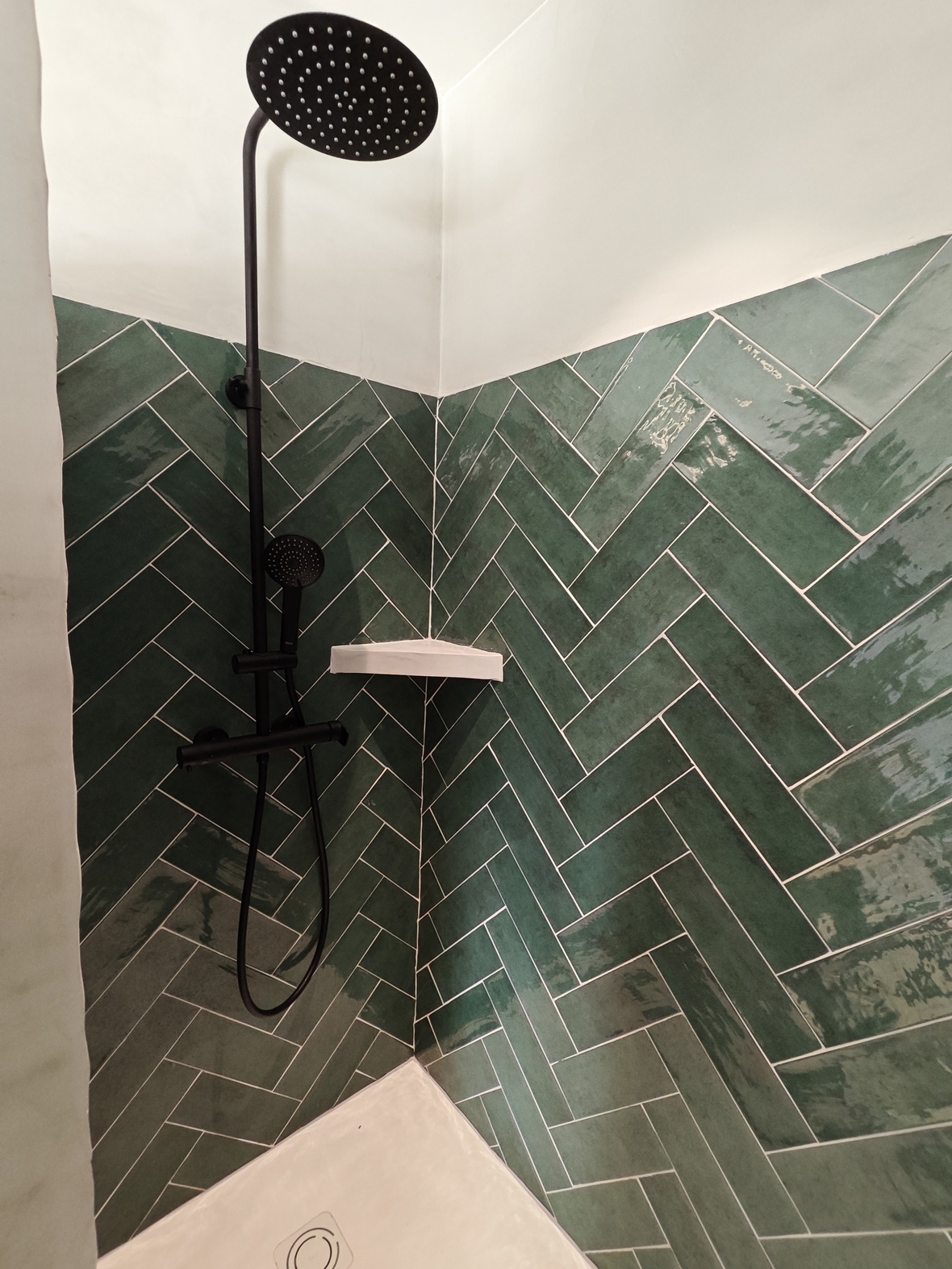 Douche contemporaine avec carrelage vert émeraude posé en chevrons, robinetterie noire mate et large pomme de douche à effet pluie.