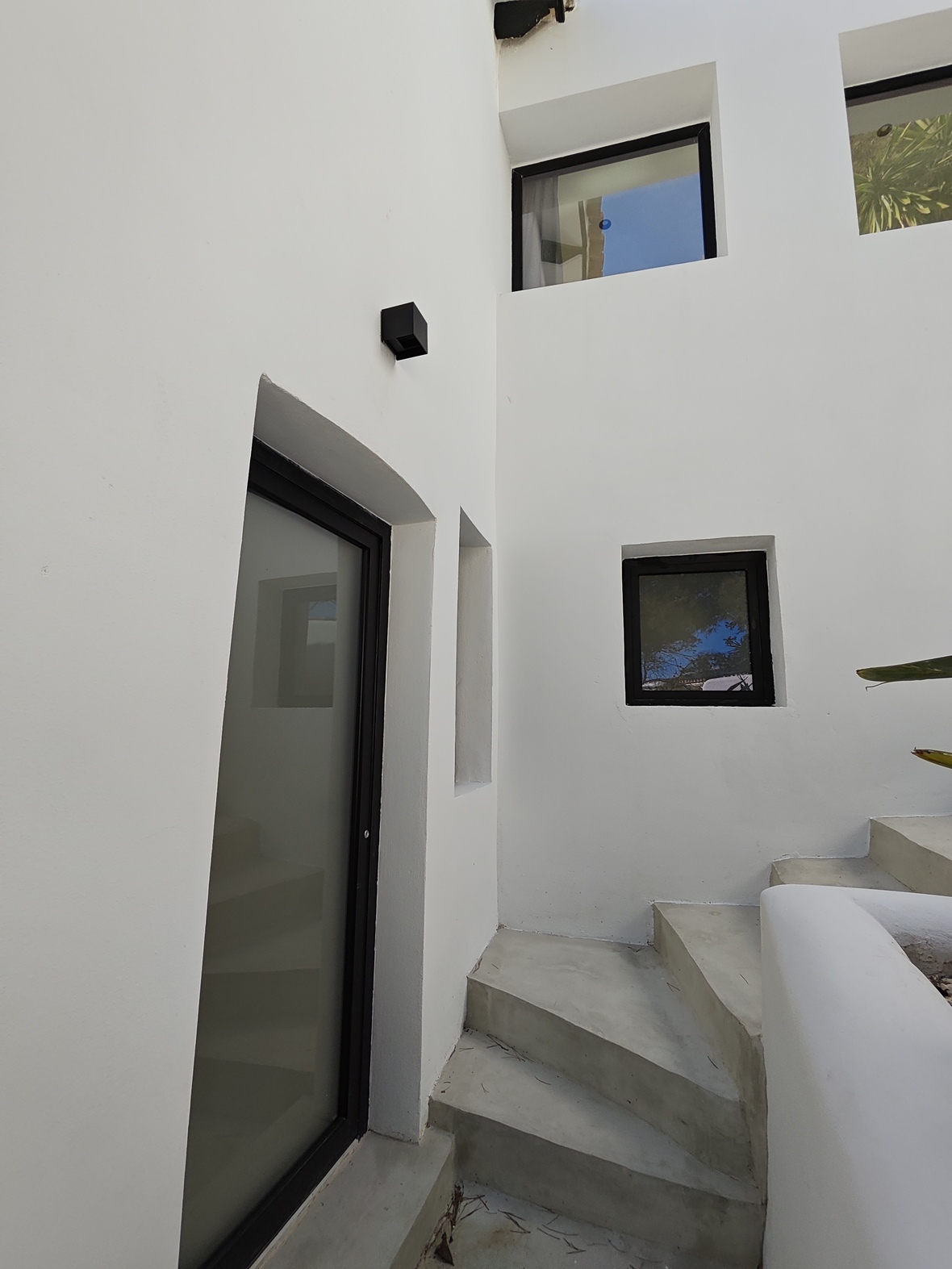 Escalier extérieur en béton bordé de murs blancs épurés, avec des fenêtres à cadre noir et une porte en verre dépoli.