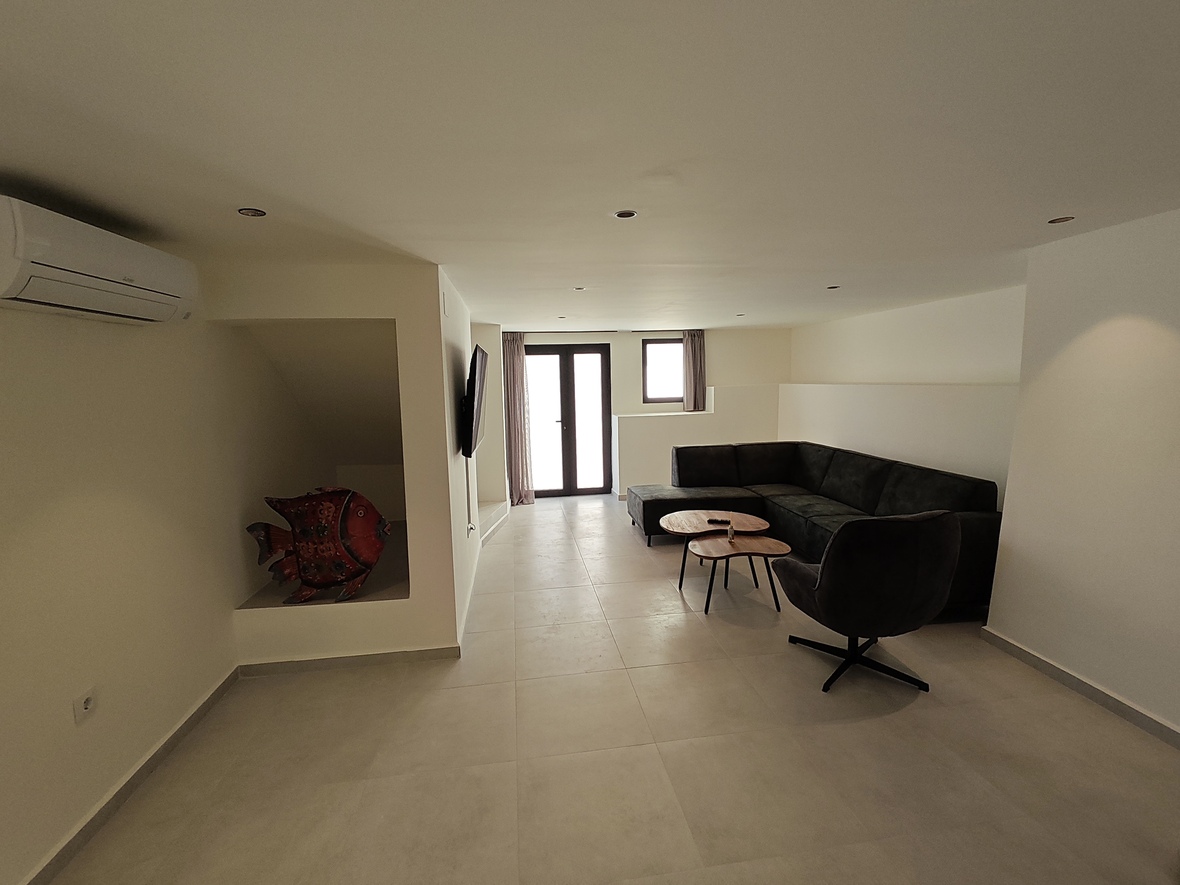 Espace de vie moderne avec canapé d'angle gris, tables en bois et niche décorative. Comprend la climatisation, des spots encastrés et un accès vers l'extérieur.