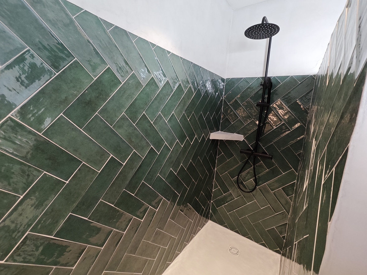 Espace douche avec carrelage vert brillant en chevrons, robinetterie noire contemporaine et receveur de douche blanc minimaliste.