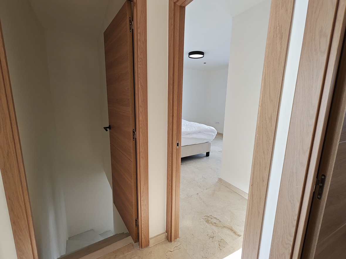 Palier avec portes en chêne et sol en pierre naturelle, offrant un accès à une chambre lumineuse et à l'escalier menant au niveau inférieur.