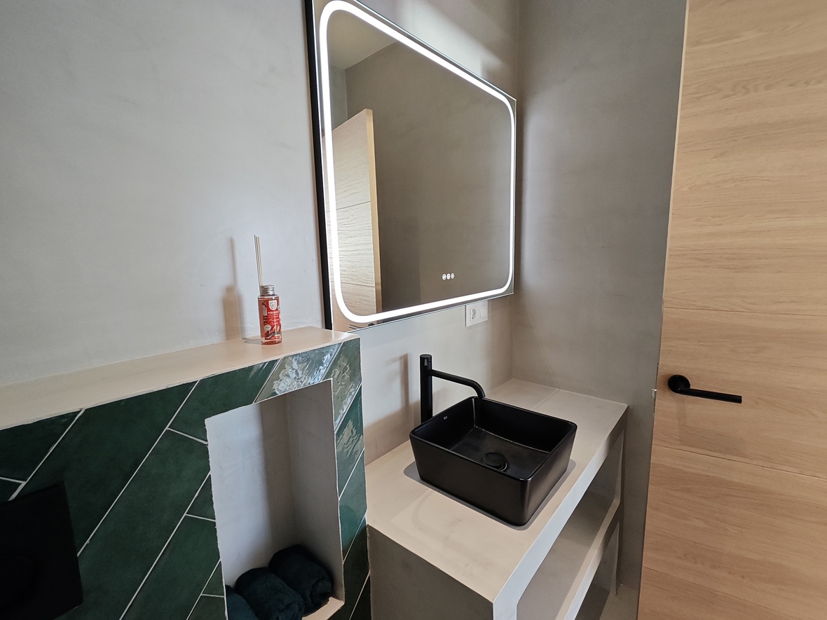 Salle de bain contemporaine avec vasque noire, miroir à éclairage LED intégré et crédence en carrelage vert posé en chevrons.