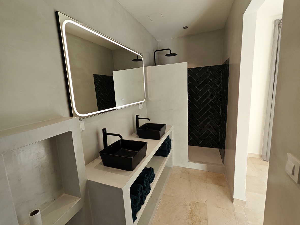 Salle de bain moderne avec double vasque en microciment, vasques noires, miroir rétroéclairé et douche à l'italienne avec carrelage noir en chevrons.