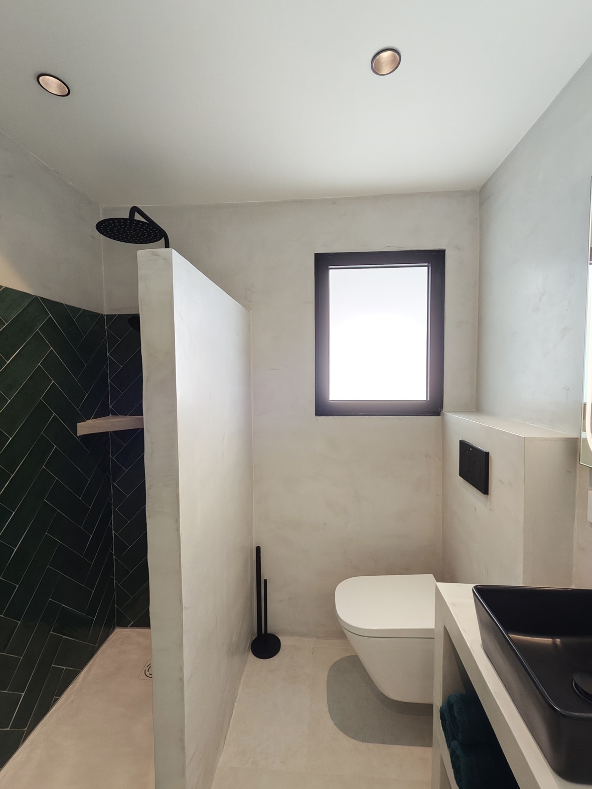 Salle de bain moderne avec douche à l'italienne en carreaux verts à chevrons, toilettes suspendues et finitions en microciment blanc.