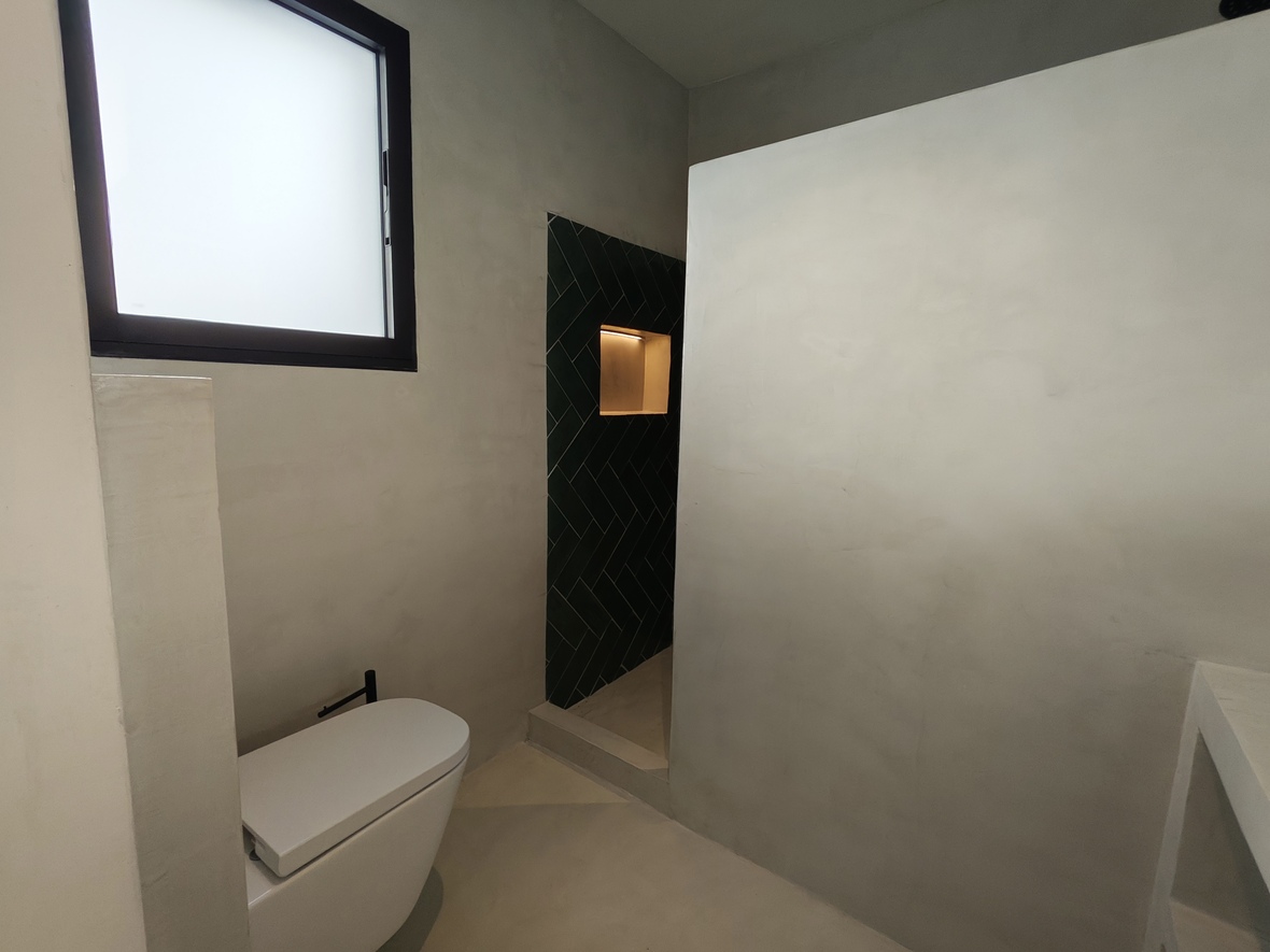 Salle de bain moderne avec murs en microciment, WC suspendu et douche à l'italienne avec carrelage vert en chevrons et niche intégrée éclairée.