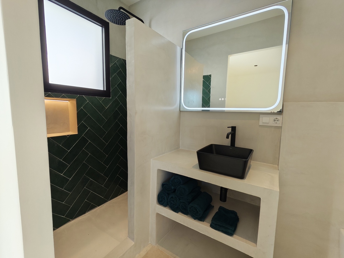 Salle de bain moderne avec vasque noire sur plan en microciment, miroir rétroéclairé et douche à l'italienne ornée de carreaux verts en chevrons.