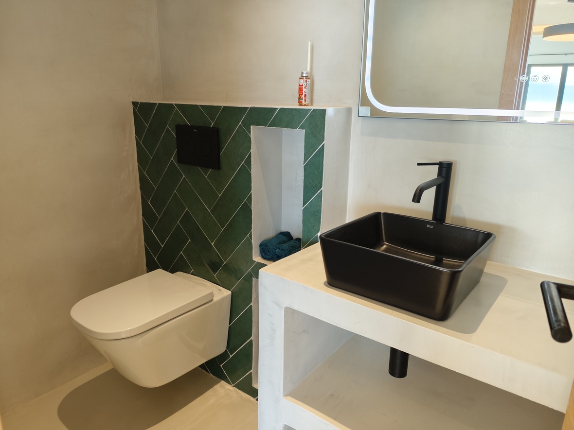Salle de bain moderne avec vasque noire sur plan en microciment, mur d'accent en carreaux verts à chevrons et WC suspendu.