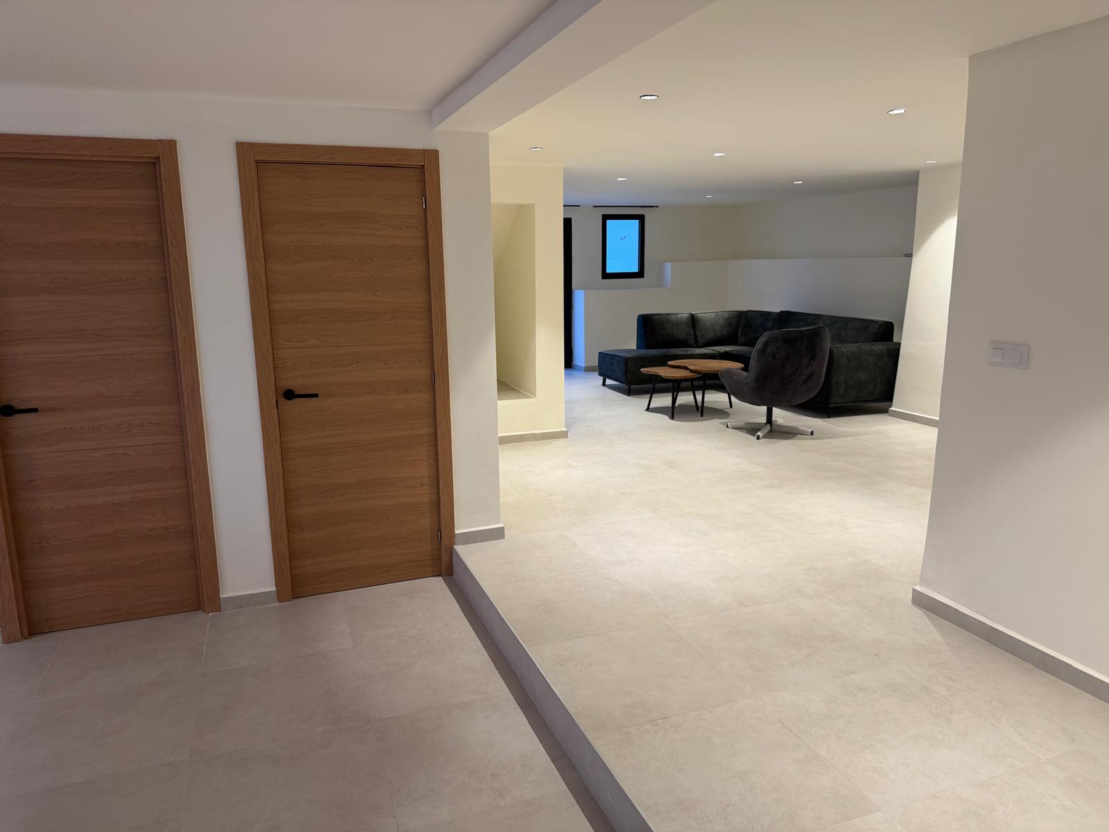 Salon contemporain avec carrelage gris clair, spots encastrés et canapé d'angle noir, agrémenté de portes en bois aux finitions naturelles.