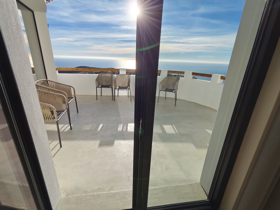 Terrasse avec vue panoramique sur la mer, dotée de chaises en corde tressée, de murs blancs avec main courante en bois et d'un sol en béton lissé.