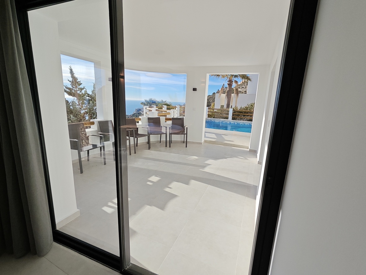 Terrasse couverte avec carrelage blanc et mobilier de jardin, offrant une vue dégagée sur la mer et l'espace piscine sous un éclairage naturel.