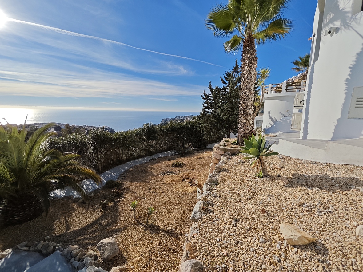 Terrasse de jardin en gravier avec palmiers et plantes succulentes, offrant une vue panoramique sur la mer Méditerranée et le littoral escarpé.