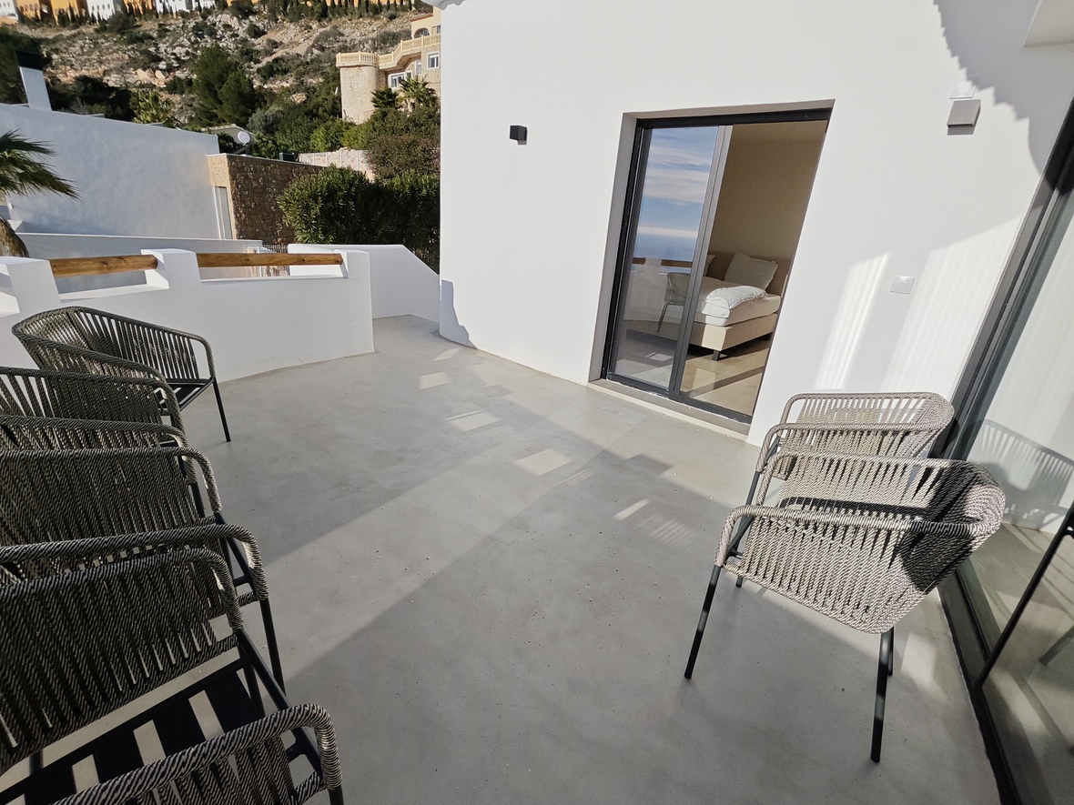 Terrasse en béton poli avec chaises en corde tressée, offrant un accès direct à la chambre par une baie vitrée coulissante.