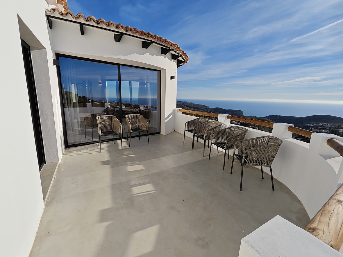 Terrasse incurvée spacieuse avec sol en microciment, fauteuils en corde tressée et vue panoramique sur la Méditerranée depuis la façade blanche.