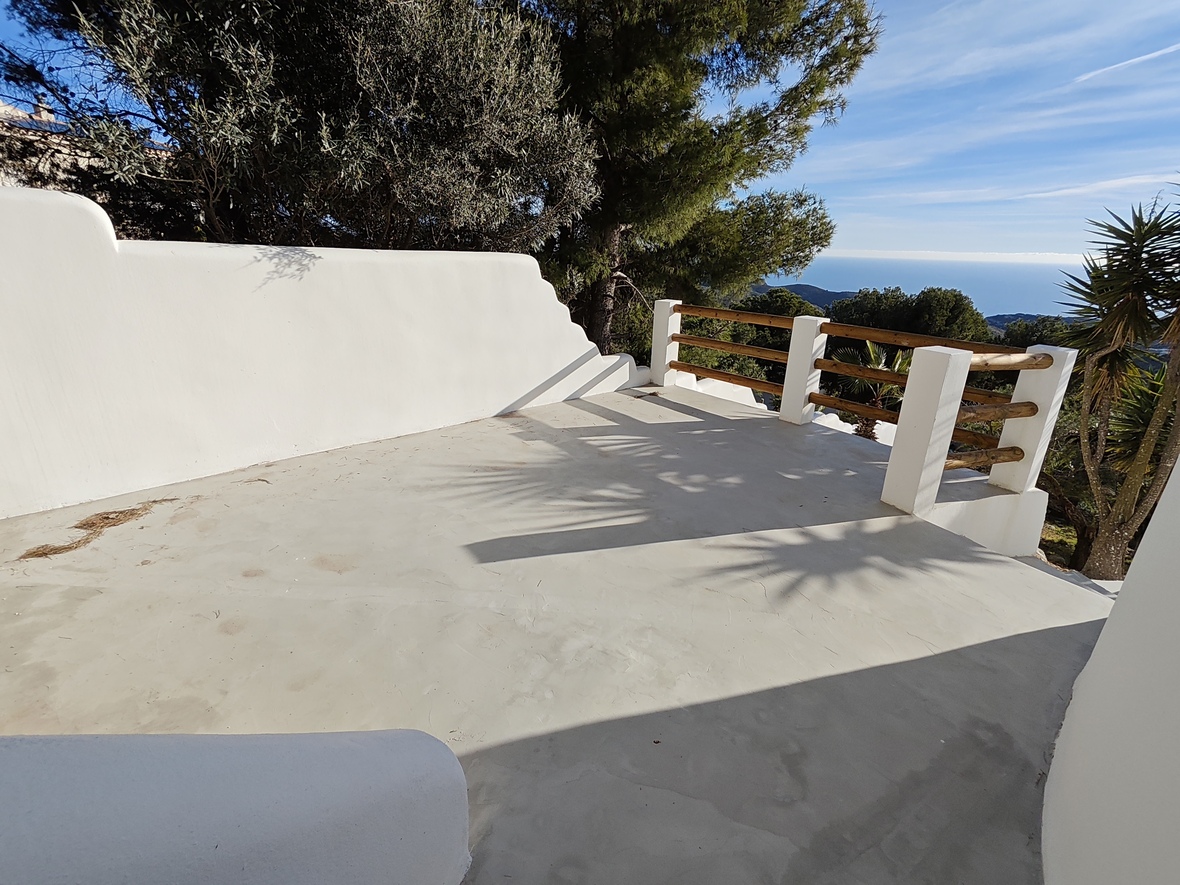Terrasse surélevée avec sol en béton lissé, murs blanchis à la chaux et garde-corps en bois offrant une vue panoramique sur la mer Méditerranée et la pinède.