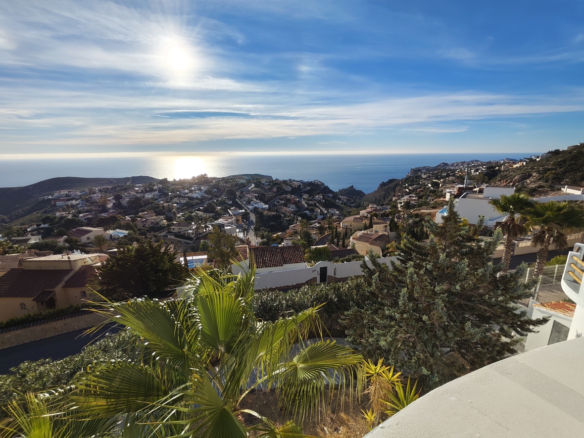 Vue panoramique surélevée sur une zone résidentielle côtière et la mer Méditerranée, avec des villas blanches, des toits en terre cuite et des palmiers.
