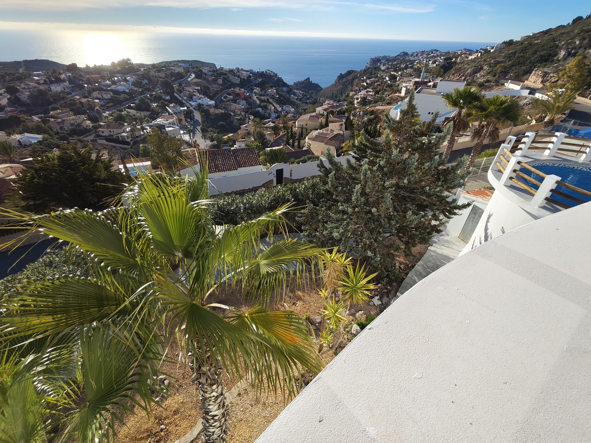Vue surélevée depuis une terrasse blanche sur une piscine circulaire, des jardins méditerranéens et un panorama dégagé sur la mer étincelante.