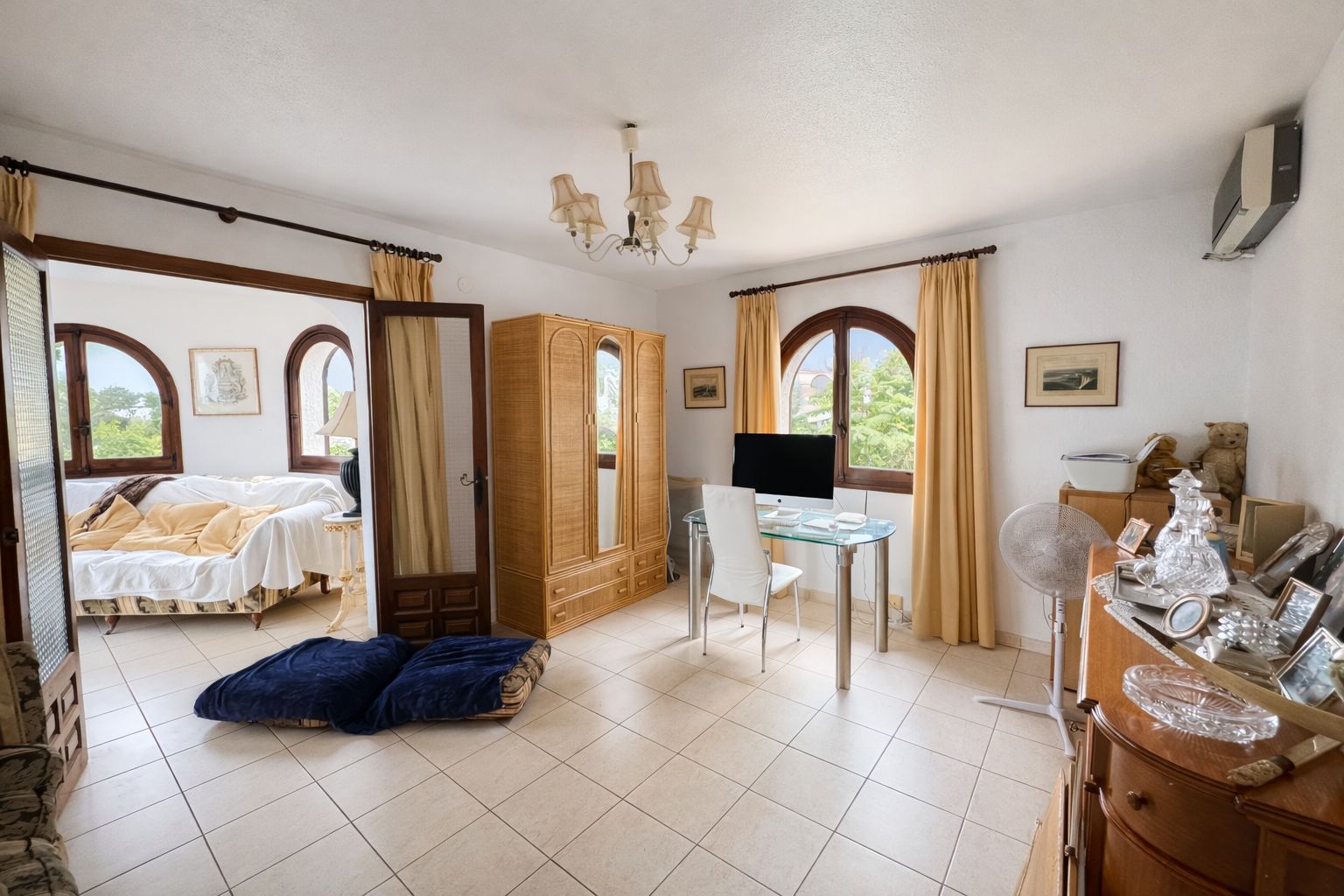 Bureau lumineux avec bureau en verre, armoire en bois et fenêtres cintrées. Comprend un sol en carrelage et un accès direct à un salon attenant.