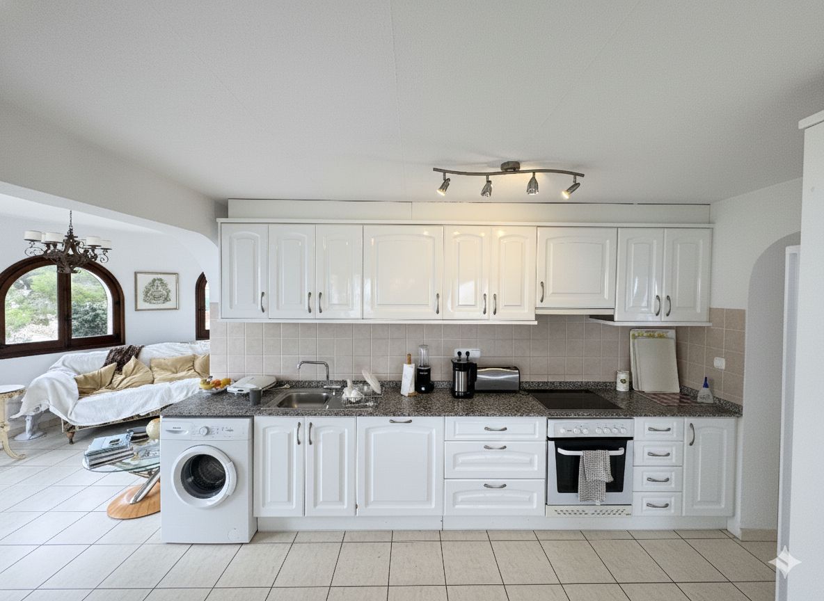 Cuisine linéaire avec placards blancs, plan de travail en granit et électroménager intégré. Elle dispose d'une crédence en carrelage beige et d'un éclairage sur rail.