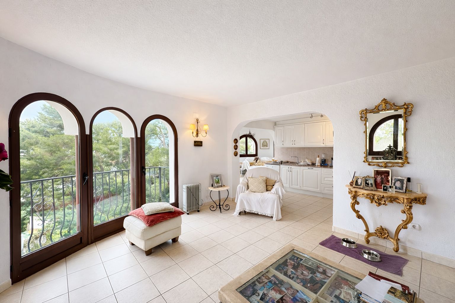Séjour lumineux doté de trois portes-fenêtres cintrées ouvrant sur un balcon, avec des murs blancs texturés et une console dorée de style classique.