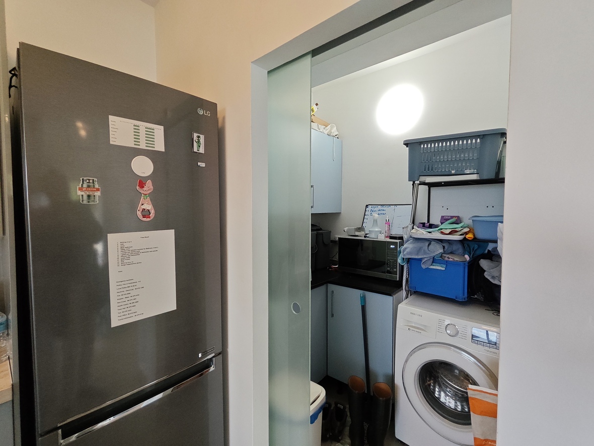 Buanderie avec porte coulissante en verre dépoli, équipée d'un lave-linge Samsung, d'un micro-ondes et de meubles bleu clair à côté d'un réfrigérateur LG.