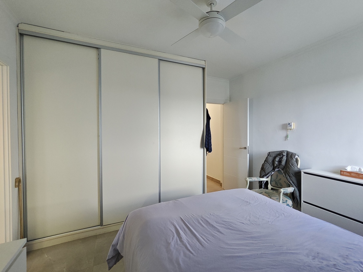 Chambre à coucher équipée d'un grand placard intégré à trois portes coulissantes, d'un ventilateur de plafond et d'un fauteuil au style classique.