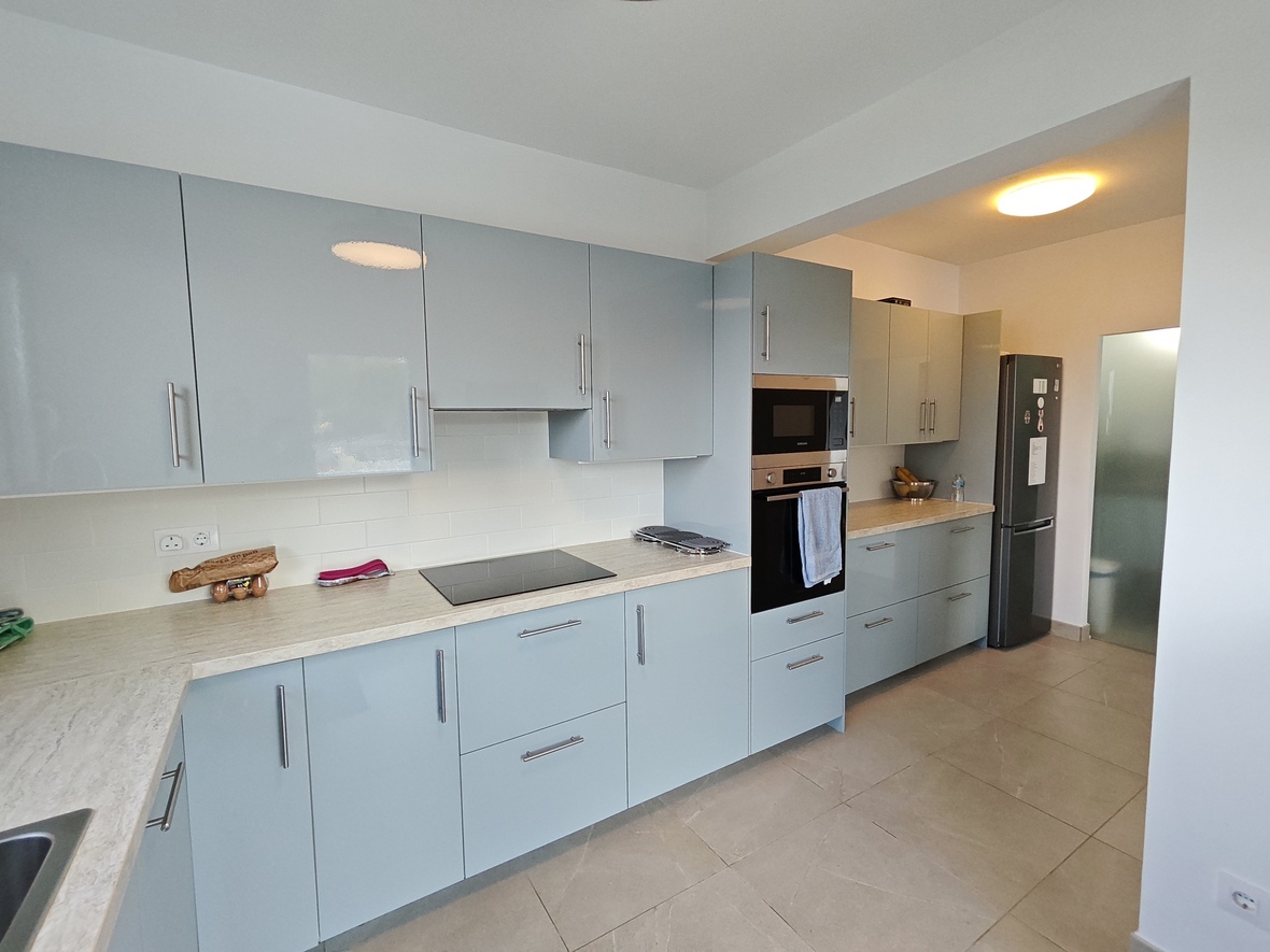 Cuisine moderne avec des meubles bleu clair brillants, un plan de travail effet pierre et des appareils intégrés sur un sol en carrelage grand format.
