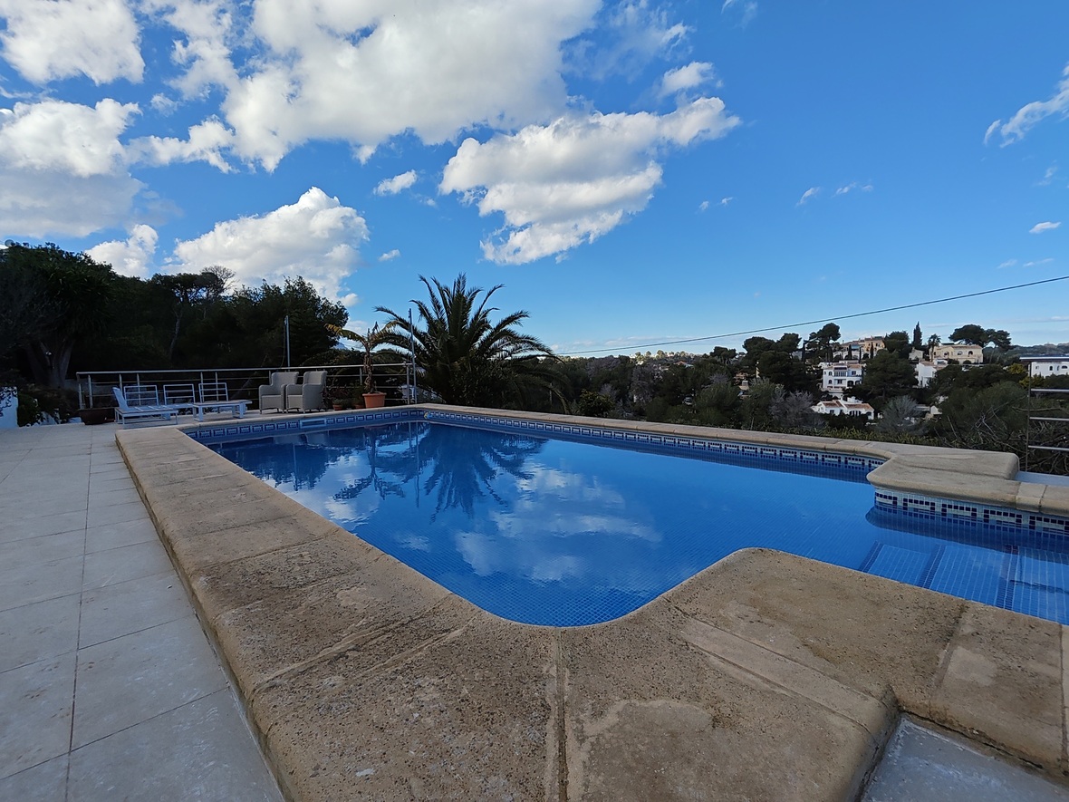 Piscine extérieure avec carrelage en mosaïque bleue et bordures en pierre, offrant une vue dégagée sur le paysage méditerranéen et les collines.