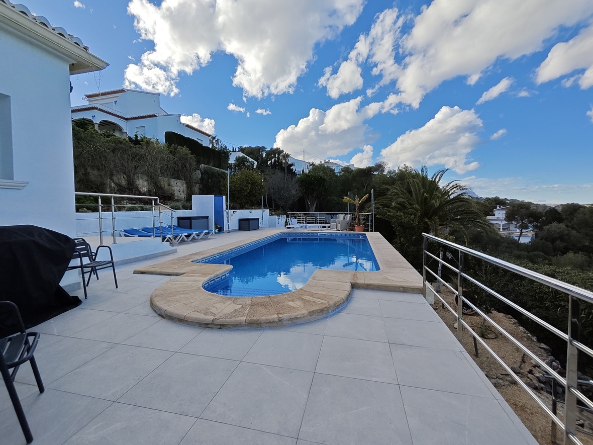 Piscine extérieure avec margelles en pierre, entourée d'une vaste terrasse carrelée et de garde-corps en inox offrant une vue dégagée sur le paysage.