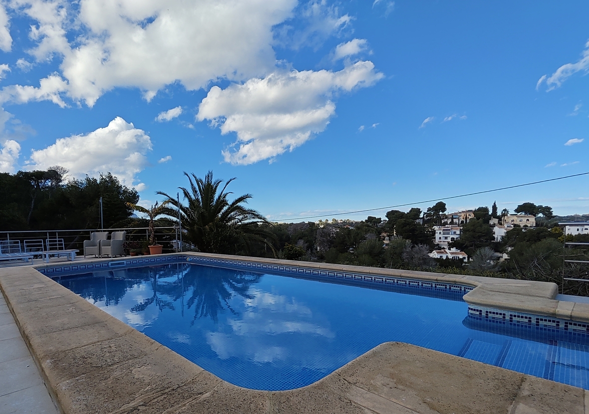 Piscine extérieure avec mosaïque bleue et bordure en pierre, offrant une vue sur le paysage résidentiel méditerranéen et la végétation environnante.