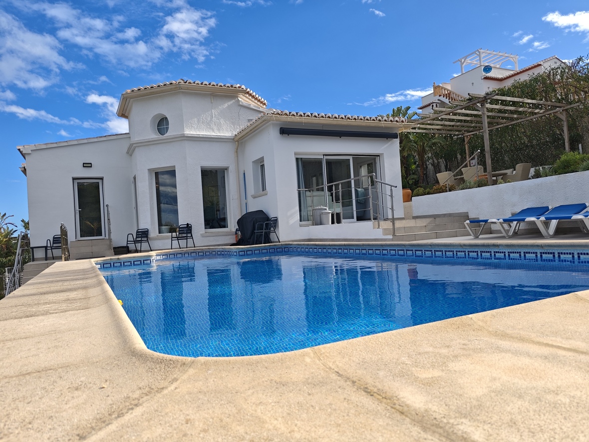 Piscine privée avec mosaïque bleue, entourée d'une terrasse en pierre et d'une villa blanche dotée d'une tour circulaire architecturale.