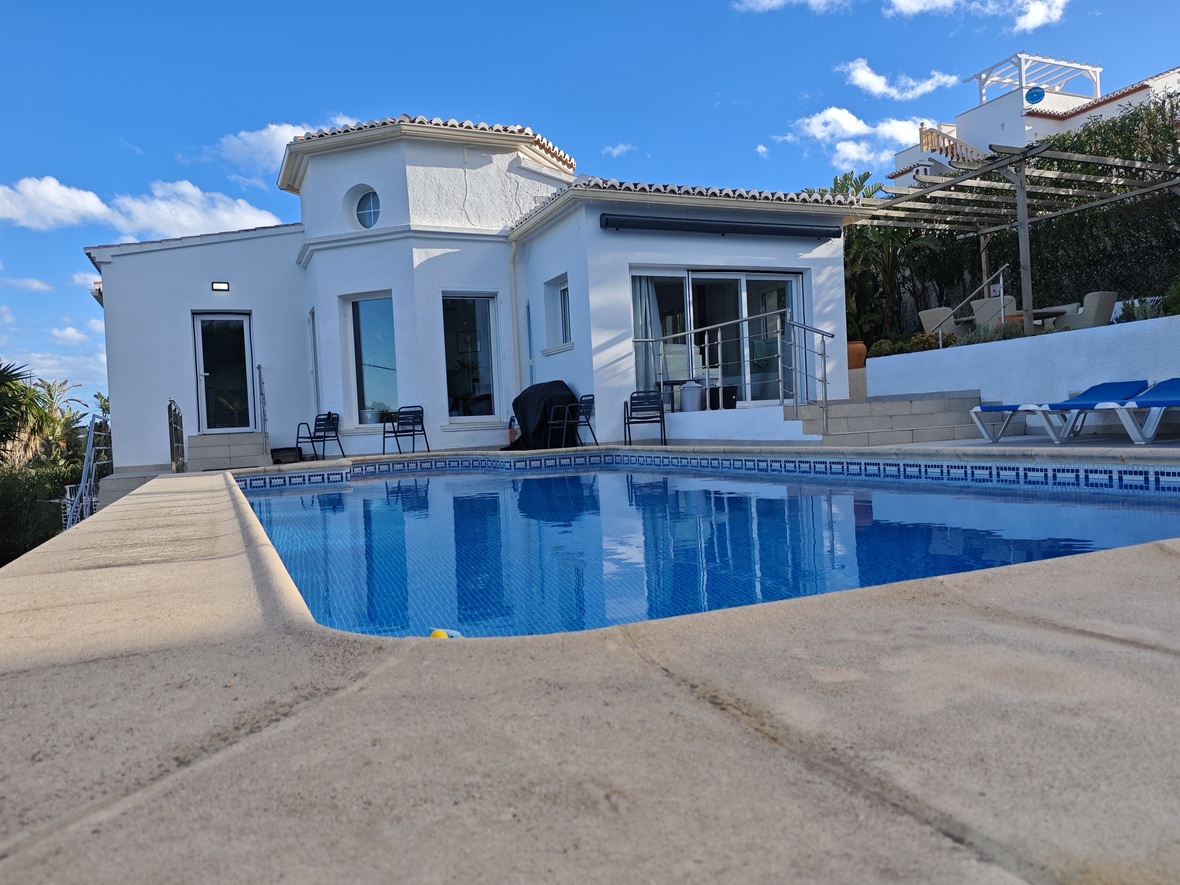 Piscine privée avec mosaïque bleue et terrasse en pierre, devant une villa méditerranéenne blanche dotée d'une tour octogonale et de larges baies vitrées.