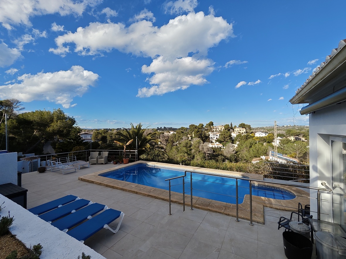 Terrasse surélevée avec piscine rectangulaire, bains de soleil bleus et garde-corps en inox offrant une vue panoramique sur la vallée boisée.