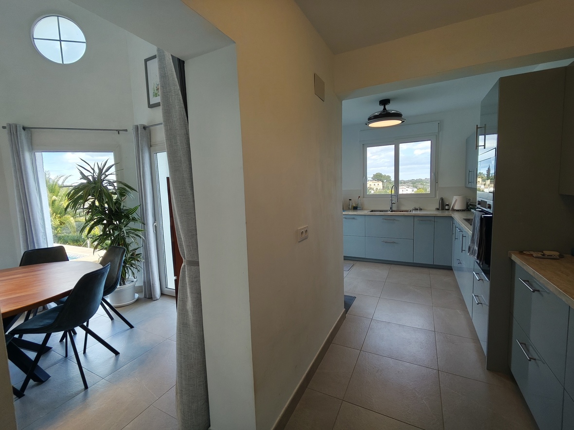 Transition entre une salle à manger lumineuse avec mobilier en bois et une cuisine moderne dotée de meubles bleu clair et d'appareils intégrés.