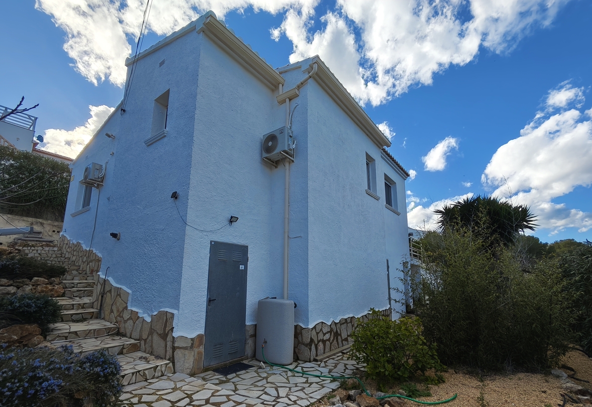 Vue extérieure de la villa présentant des murs blancs texturés, un soubassement en pierre naturelle et des installations techniques en façade.