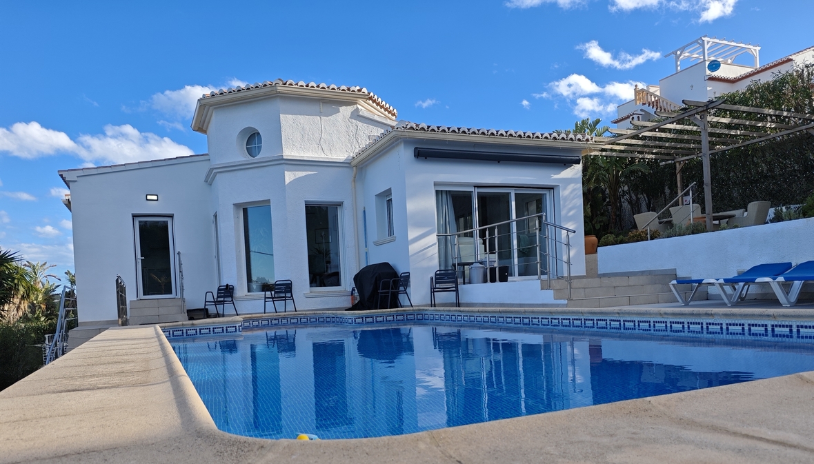 Vue extérieure d'une villa méditerranéenne blanche avec piscine privée, terrasse ensoleillée équipée de transats et pergola en bois.