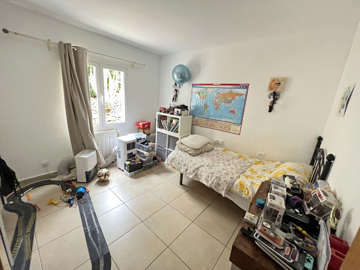 Chambre avec sol en carrelage, radiateur et fenêtre apportant une lumière naturelle. L'espace présente des murs blancs et une disposition fonctionnelle.