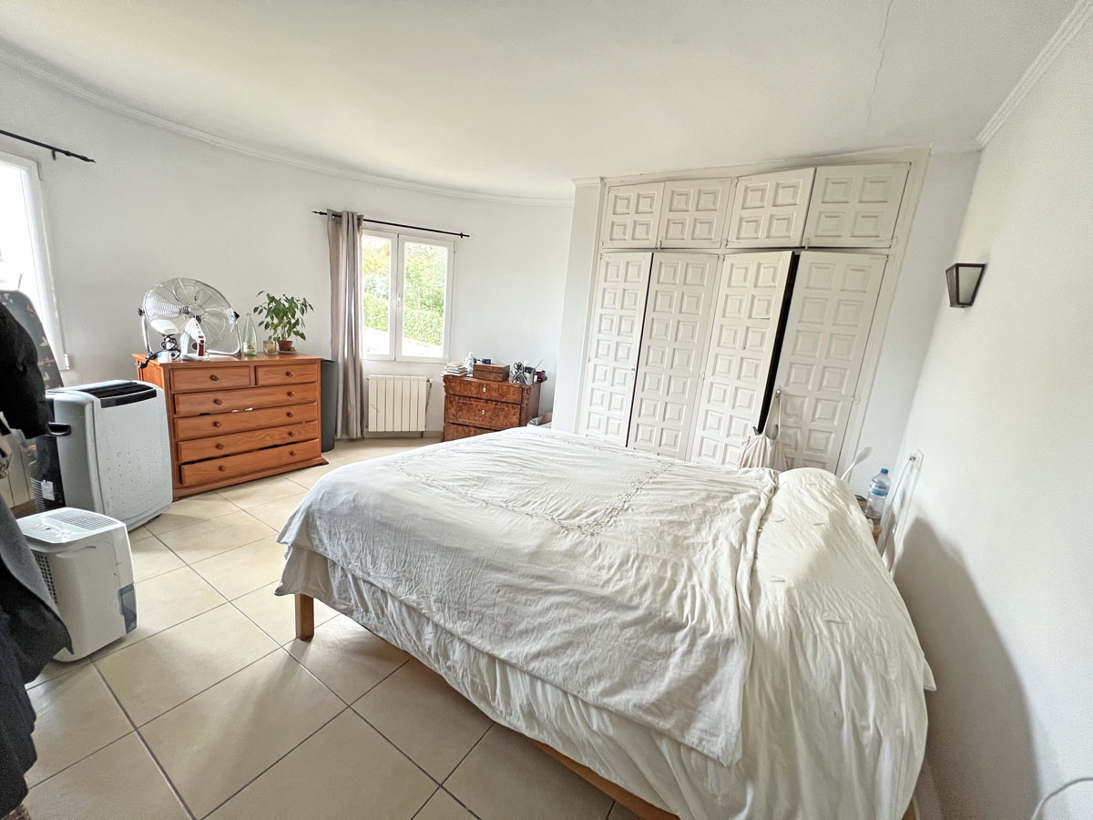 Chambre lumineuse avec de grands placards encastrés à panneaux, un sol en grès cérame et du mobilier en bois naturel sous une lumière douce.