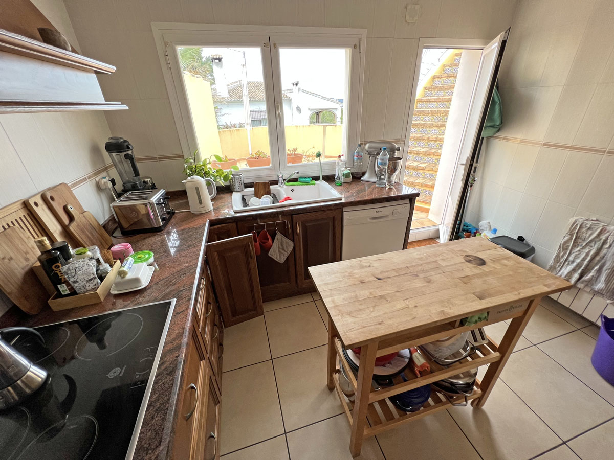 Cuisine indépendante avec plans de travail en granit, meubles en bois et îlot central mobile. Une porte donne accès à un escalier extérieur carrelé.