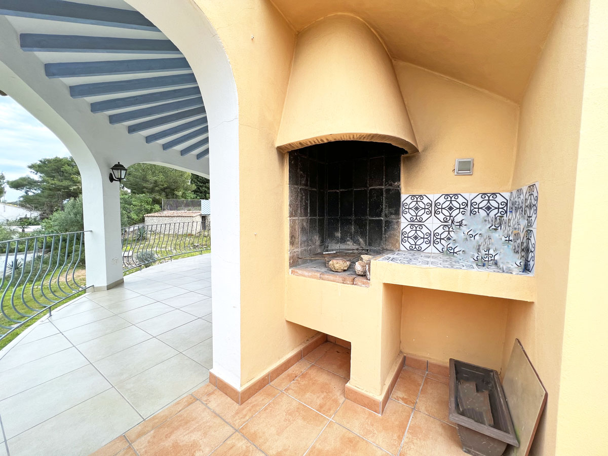 Espace barbecue maçonné sur la terrasse, comprenant un plan de travail en carrelage décoratif, une hotte intégrée et une vue sur le jardin sous les arches.